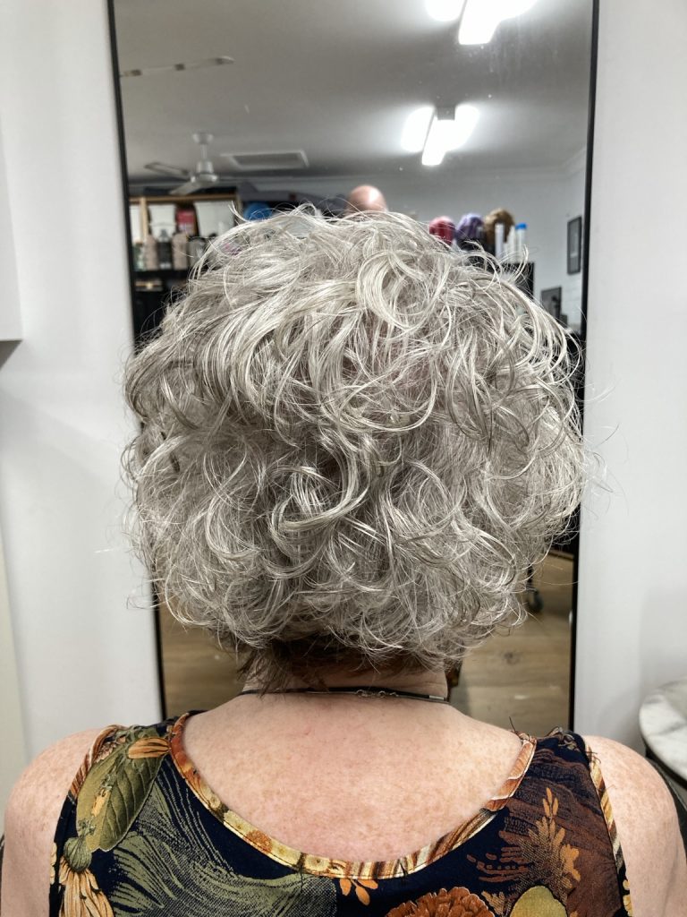After the curly haircut: short silver curls with a compact, rounded shape, viewed from the back.